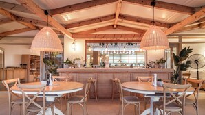 Un espace repas avec des tables et des chaises en bois, un bar central avec des verres et des luminaires suspendus.
