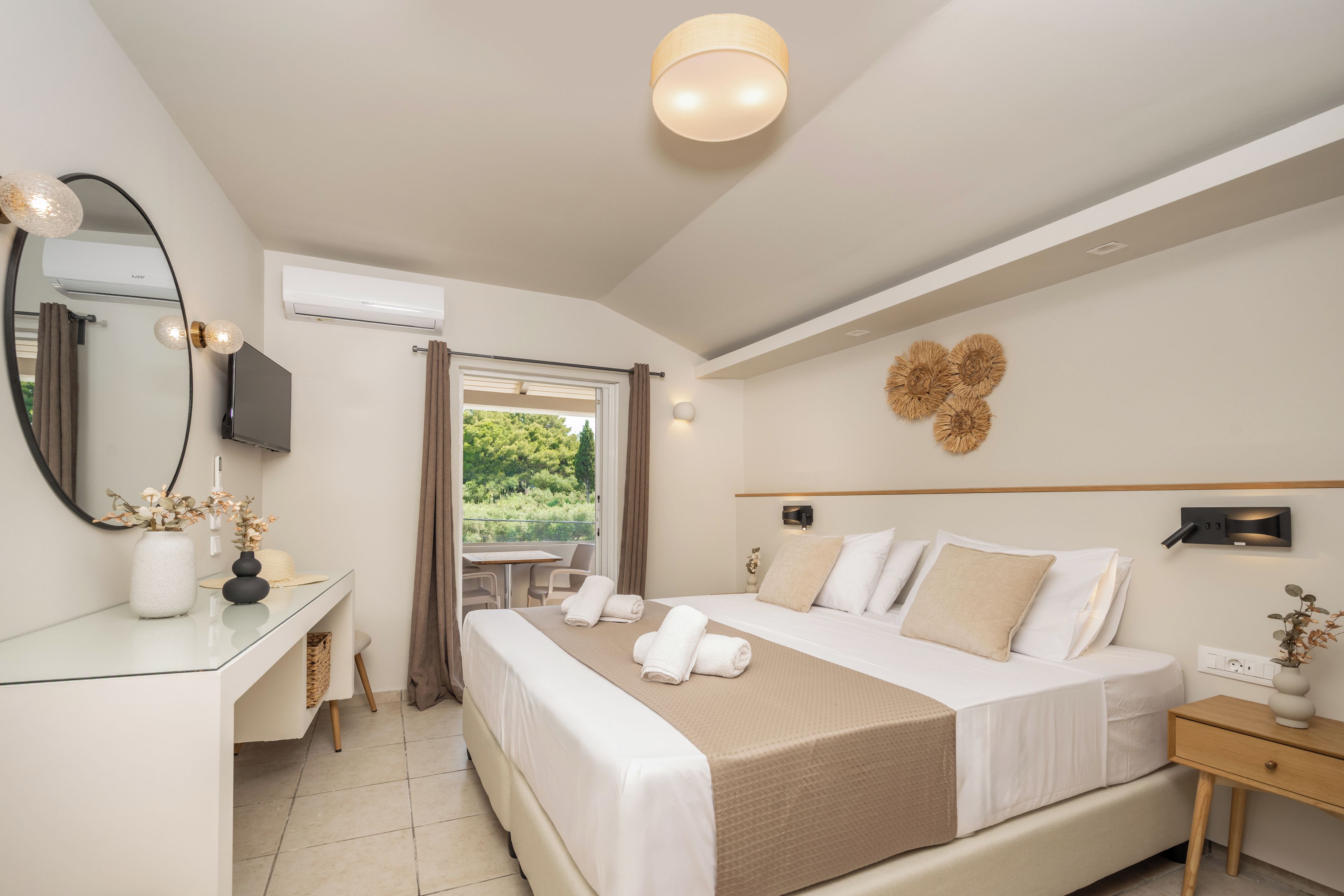 A hotel room with a bed, bedside table, mirror, and a view of the outdoors.