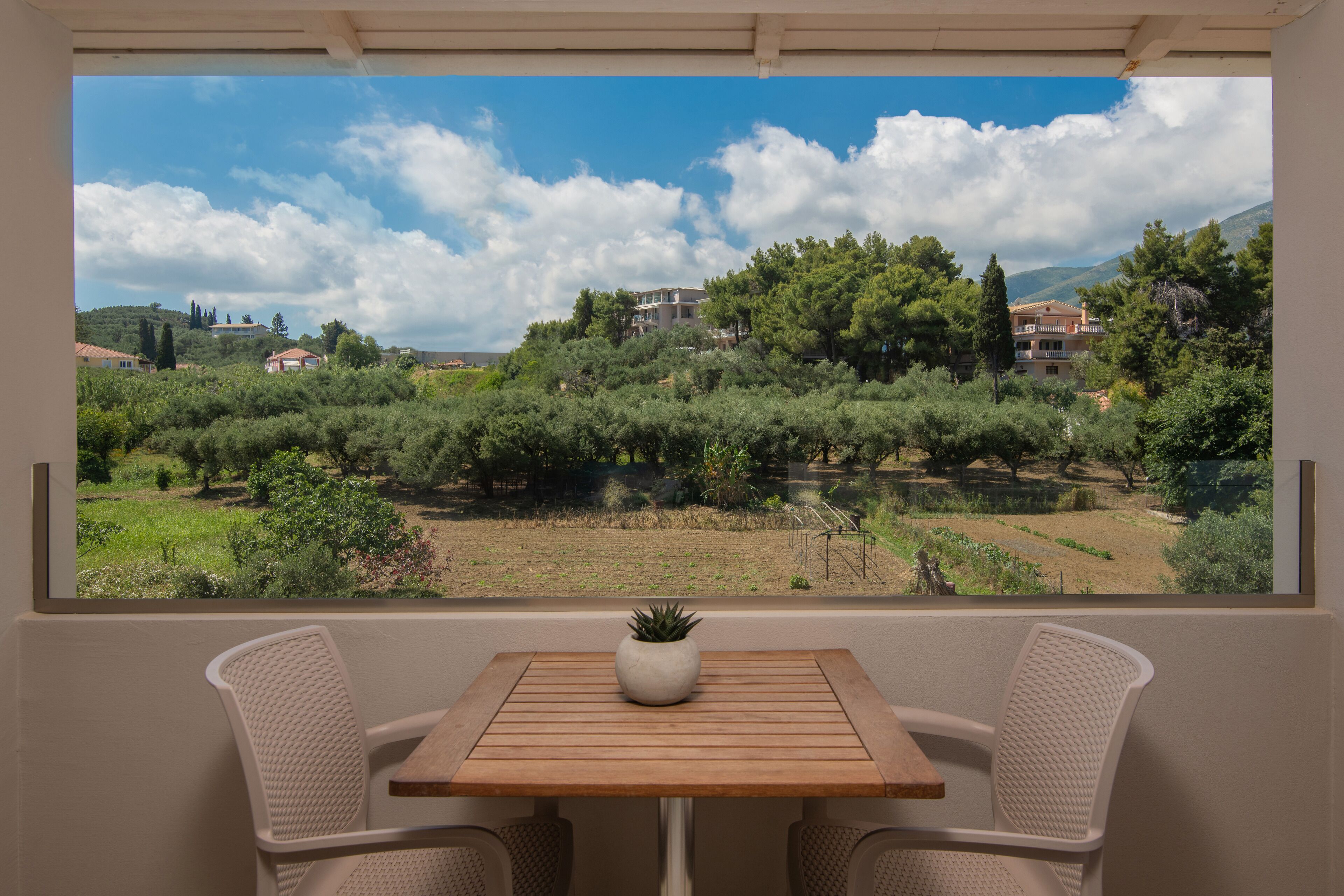 A balcony with a table and two chairs, overlooking a vineyard and buildings in the distance.
