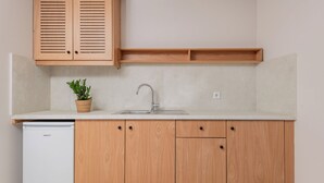 Une cuisine avec des meubles en bois, un plan de travail blanc, un évier en acier inoxydable et une petite plante en pot.
