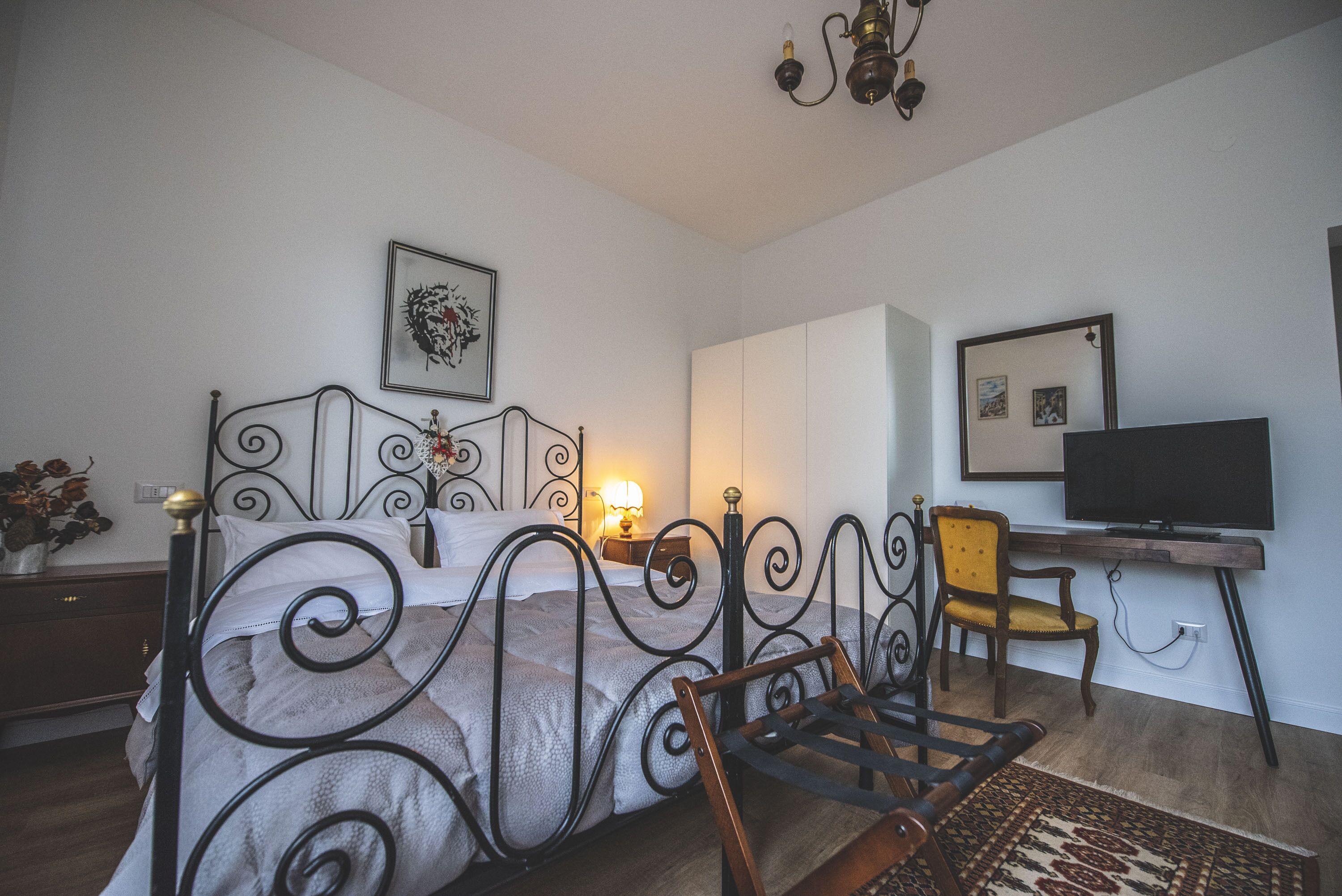 A bedroom with a metal bed frame, a wooden rocking chair, a desk with a chair, and a television.
