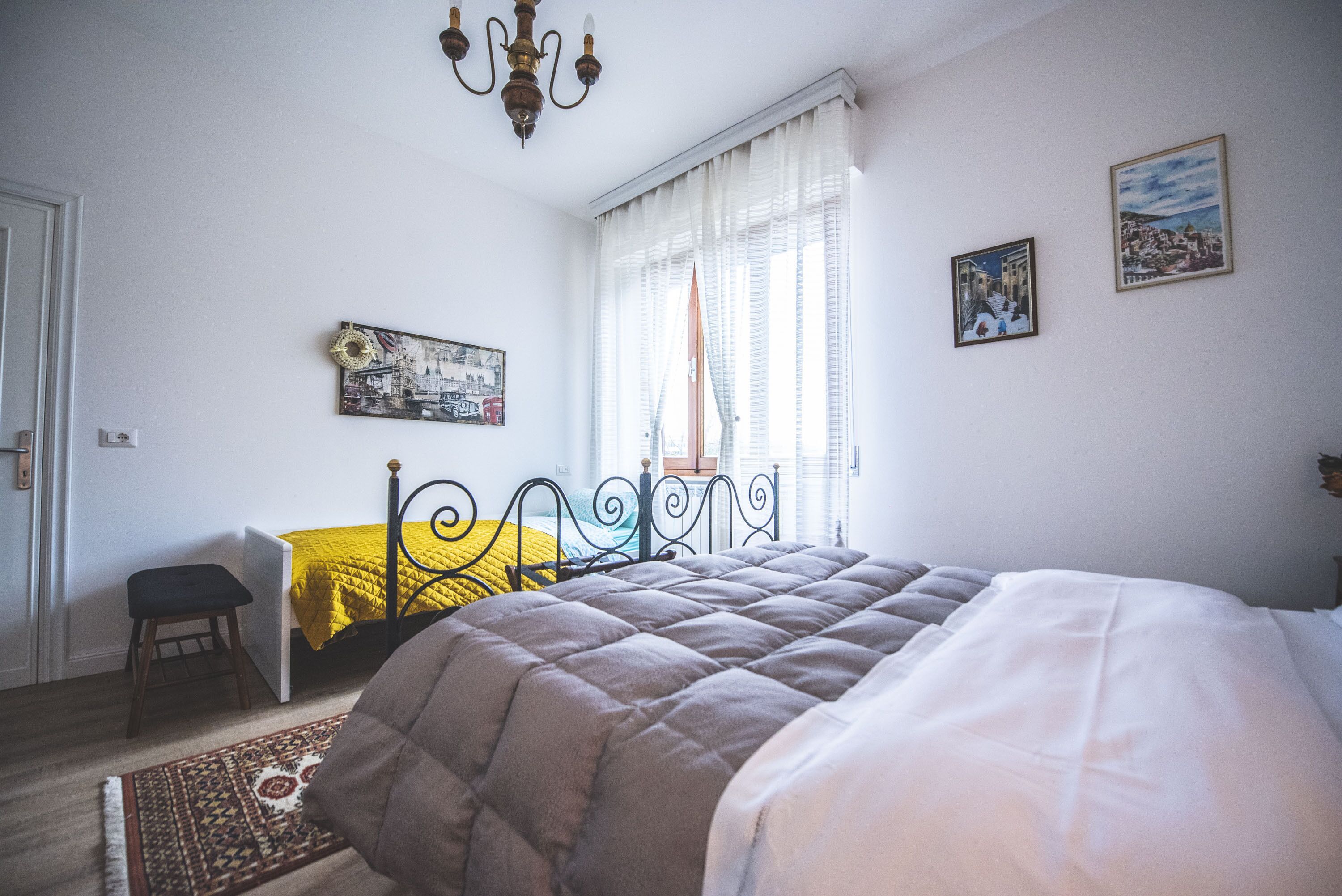 A bedroom with a bed, a chair, a window with curtains, and wall art.