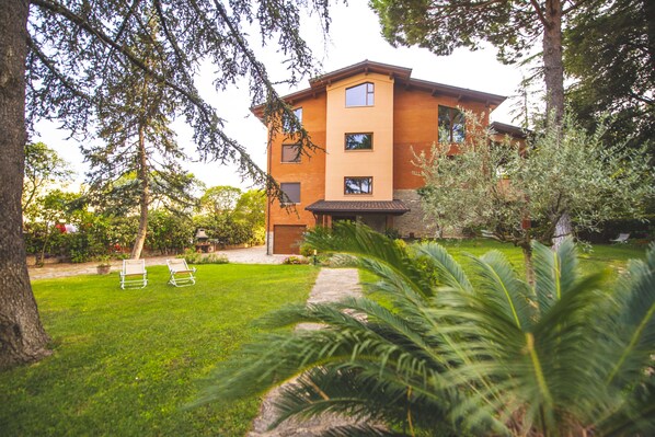 A modern two-story house with a well-maintained lawn and two lounge chairs. - B&B Il Girasole (Corciano)
