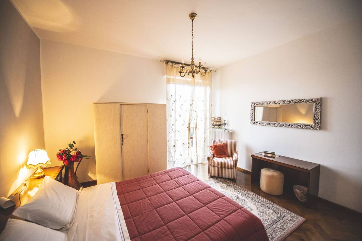 Une chambre à coucher comprenant un lit, une table de chevet, une lampe, une commode, une chaise, un miroir et un tapis.