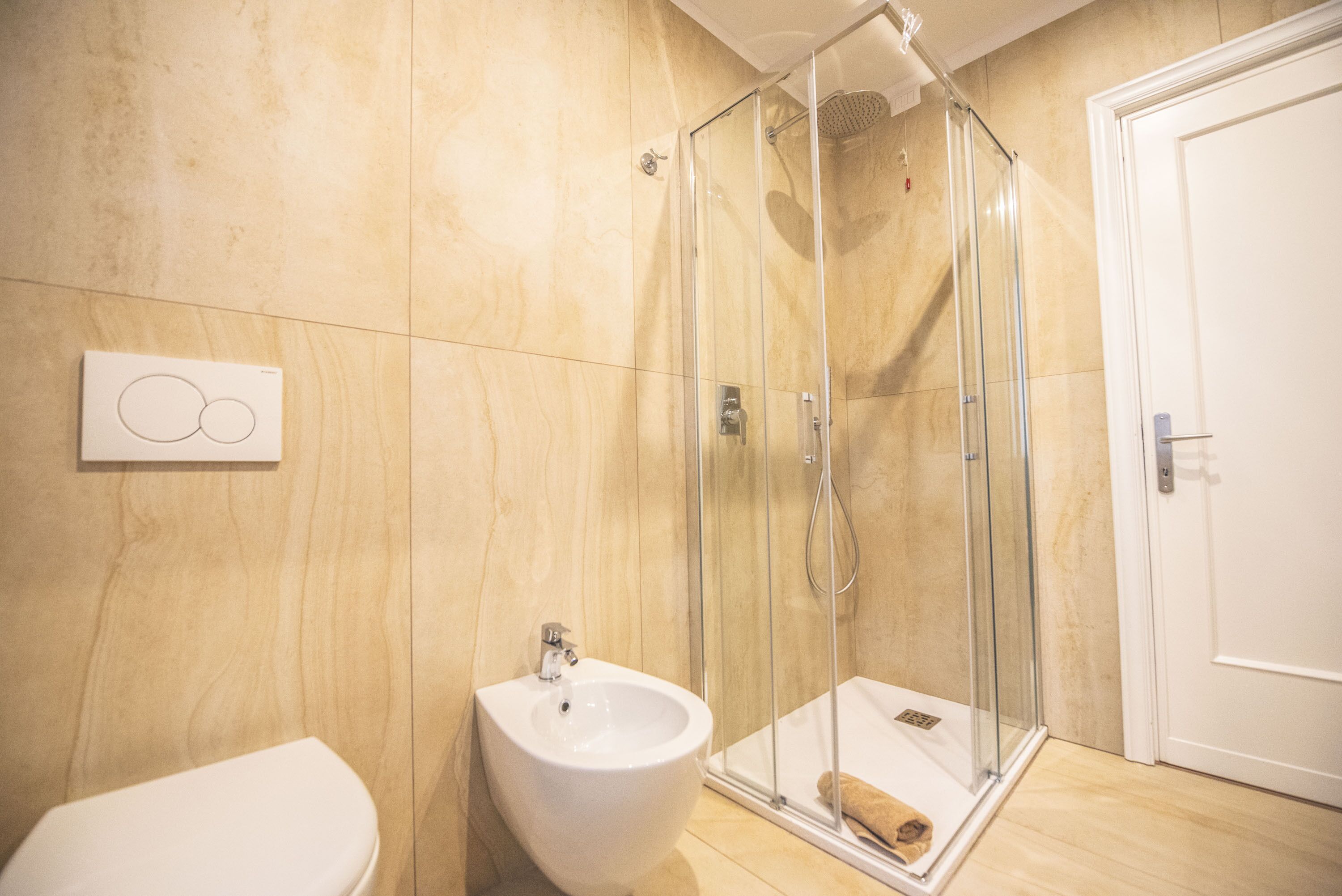 A modern bathroom with a glass-enclosed shower, a white bidet, and a wooden floor.