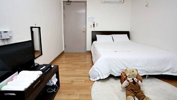 A hotel room with a bed, a television, a teddy bear, and a suitcase.