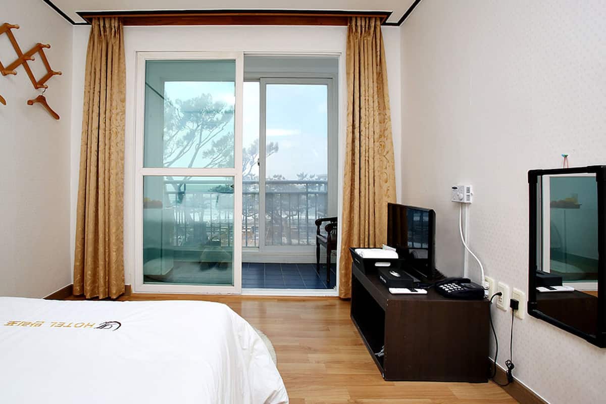 Habitación de hotel con cama, escritorio con computadora, televisor y puerta corrediza de vidrio a un balcón.