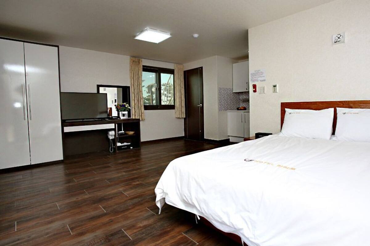 Habitación de hotel con una cama grande, un escritorio con computadora, armario y una kitchenette pequeña.