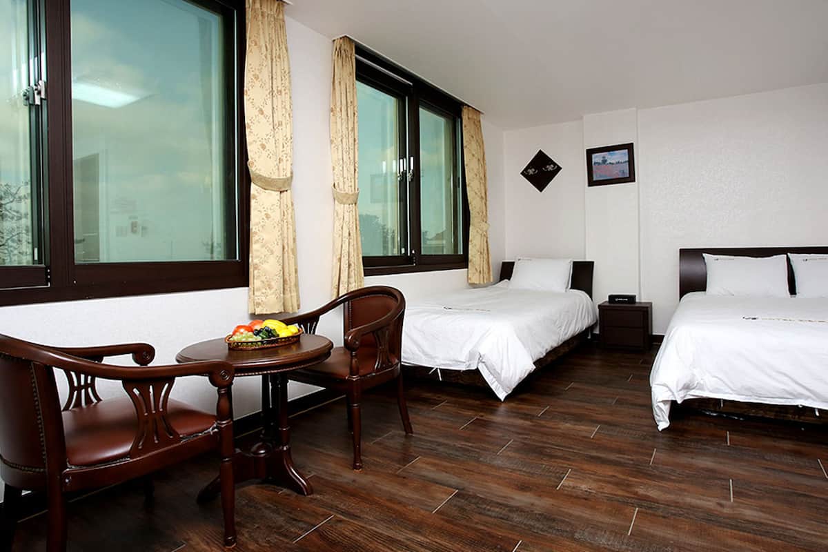 Habitación de hotel con dos camas, una silla de madera, una mesita con fruta y una ventana con cortinas.