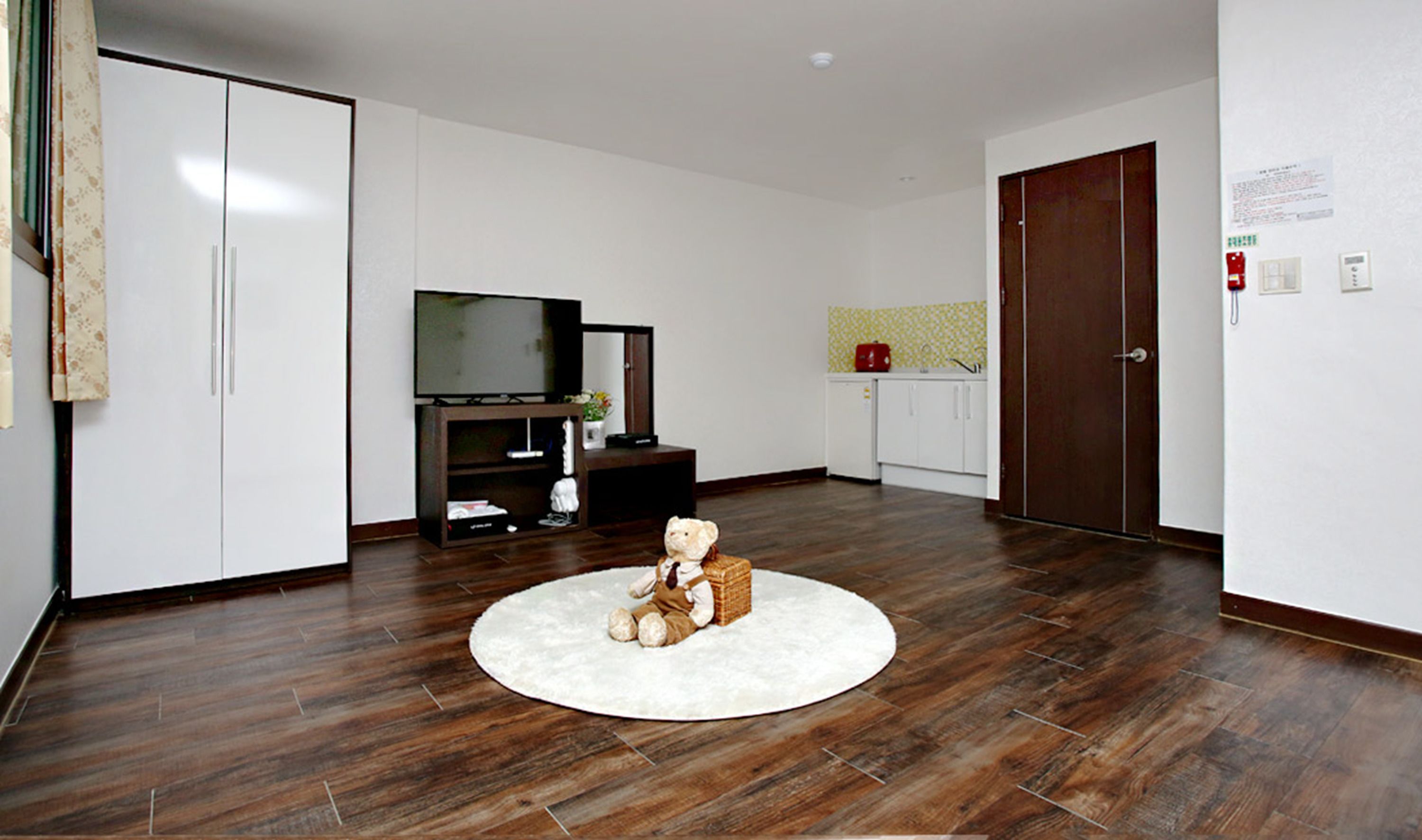 A room with a wooden floor, a television on a stand, a white cabinet, and a teddy bear on a rug.