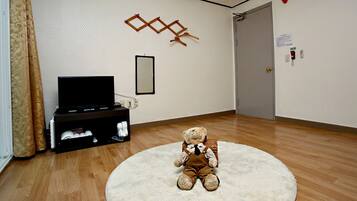 A room with a wooden floor, a white rug, a television on a stand, a teddy bear on the rug, and a door with a lock.