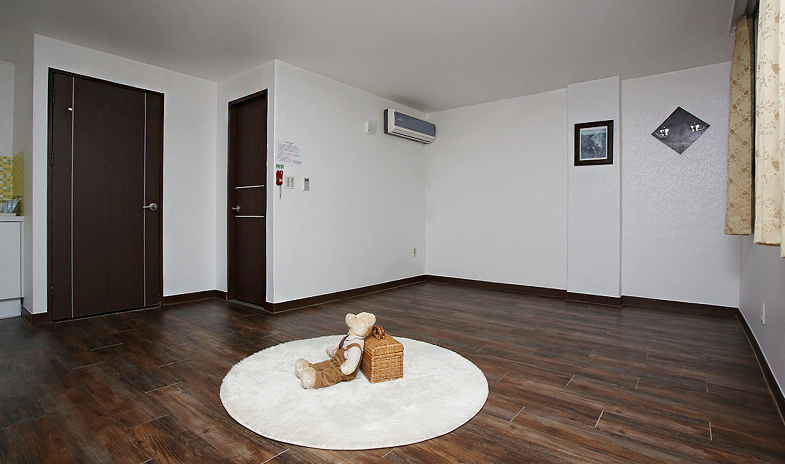 A room with a wooden floor, a white rug, a teddy bear, a wicker basket, and a door.