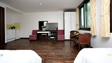 A hotel room with two beds, a desk with a TV, a small kitchenette, and a window with curtains.