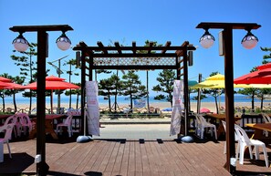 A wooden deck with tables and chairs, a pergola with hanging lights, and beach umbrellas. - Manripo Hotel (Taean)