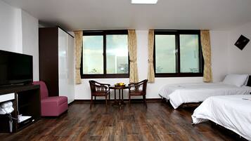 A hotel room with a TV, a pink chair, a dining table with chairs, and two beds.