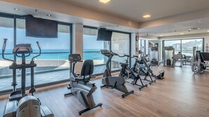 Un gimnasio moderno con diversos equipos de ejercicio, amplias ventanas con vistas al océano y un diseño espacioso.