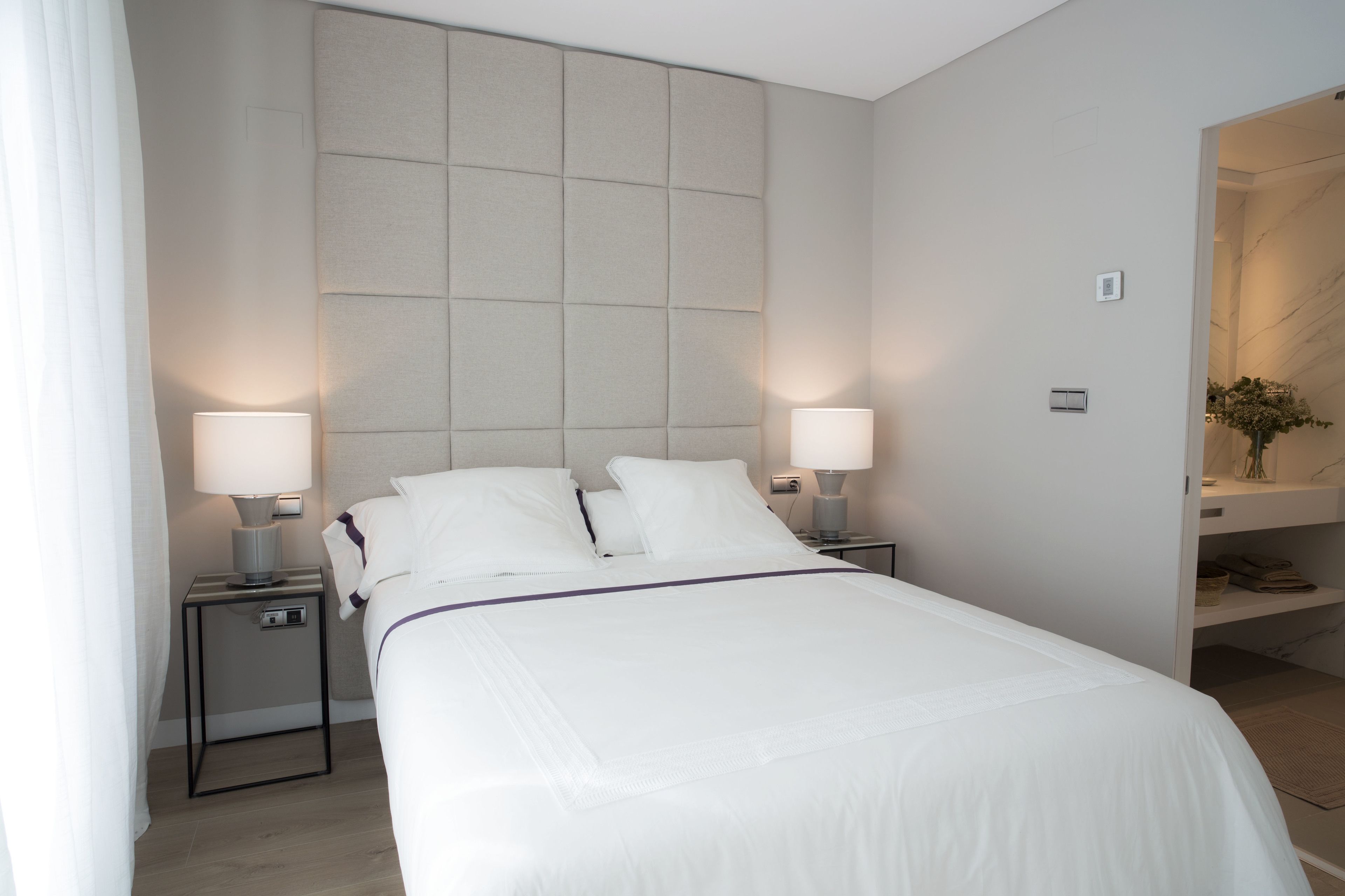 Ein modernes Hotelzimmer mit einem großen Bett, zwei Nachttischen mit Lampen, einer Kopfteil und einer eingebauten Ablage mit einer Vase.