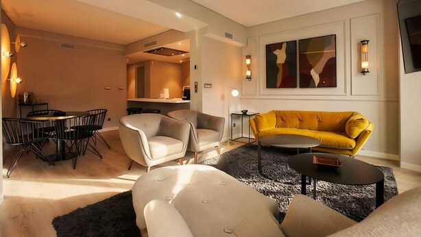 Ein modernes Wohnzimmer mit einer Couch, Sesseln, einem Couchtisch und einem Essbereich mit Tisch und Stühlen.