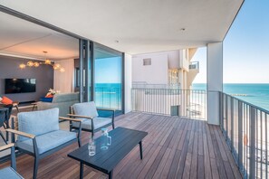 Uma varanda com piso de madeira, uma mesa preta e duas cadeiras azul claras.