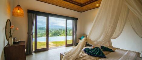 A bedroom with a large bed, a canopy, a view through a sliding door, and a wicker lamp.