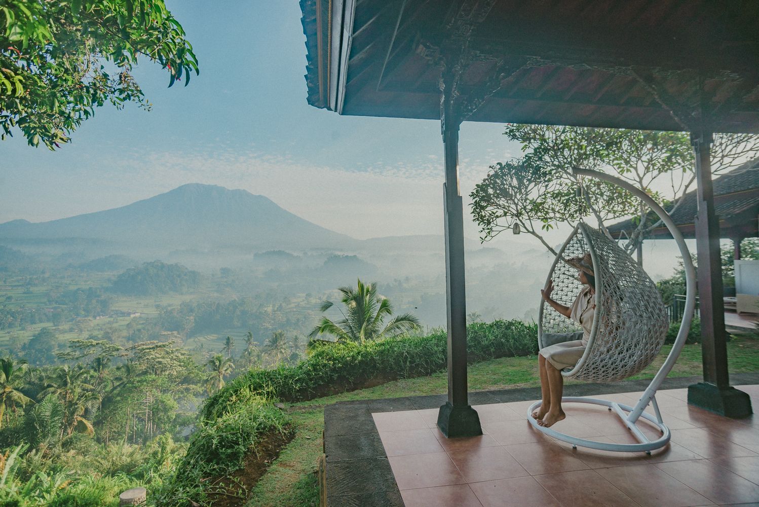 A person sitting in a hanging chair on a porch overlooking a mountainous landscape.
