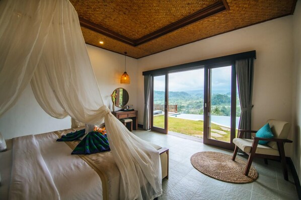 A bedroom with a canopy bed, a desk, and a view of the outdoors.