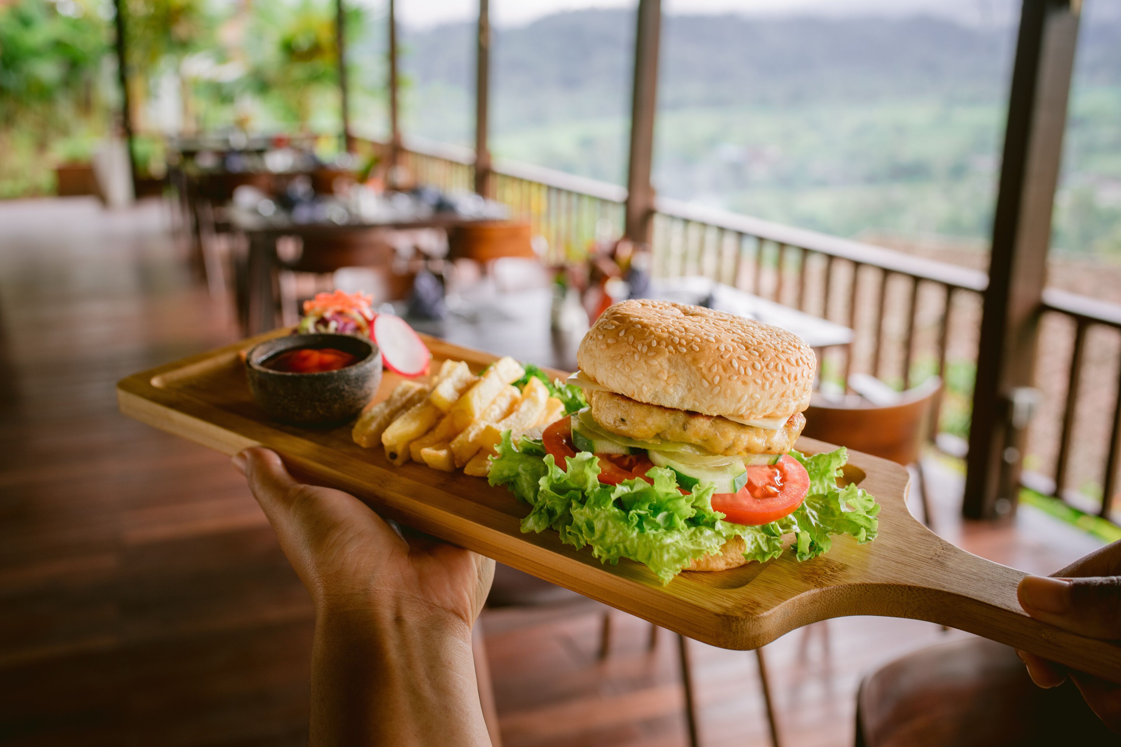 A wooden serving tray with a burger, fries, and a side salad.