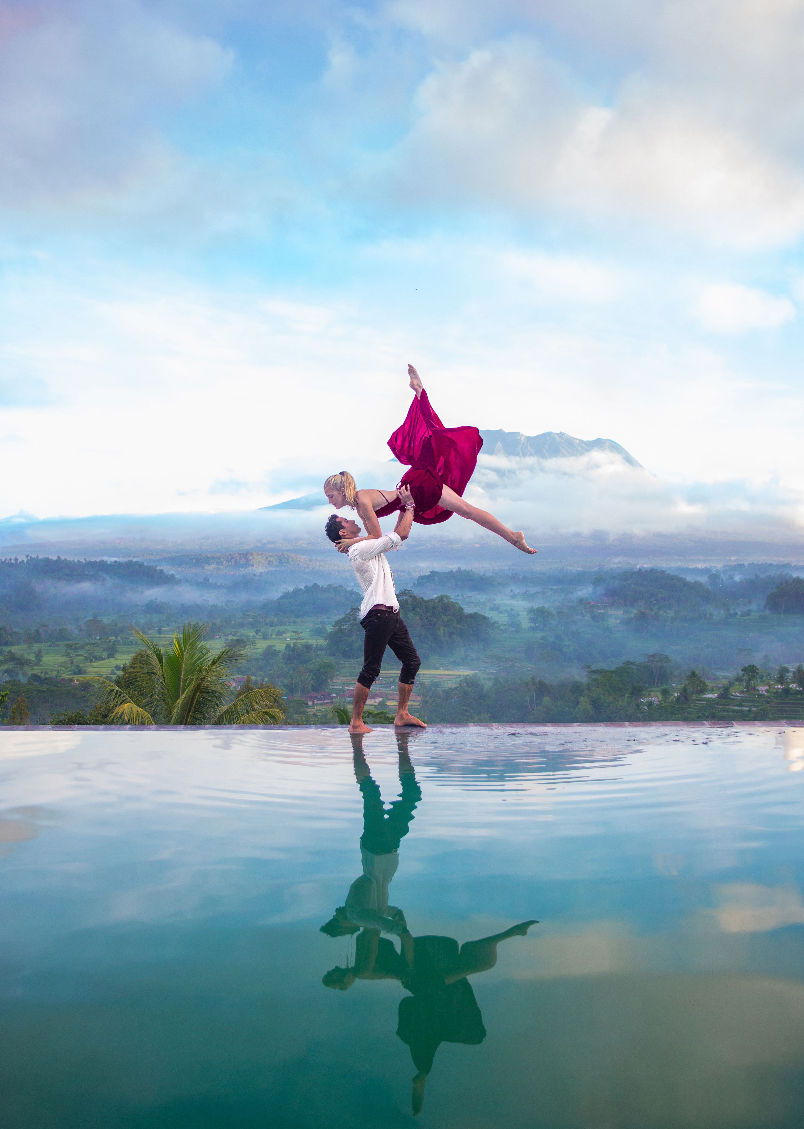 A couple performing a dance on a reflective pool with a mountainous landscape in the background.