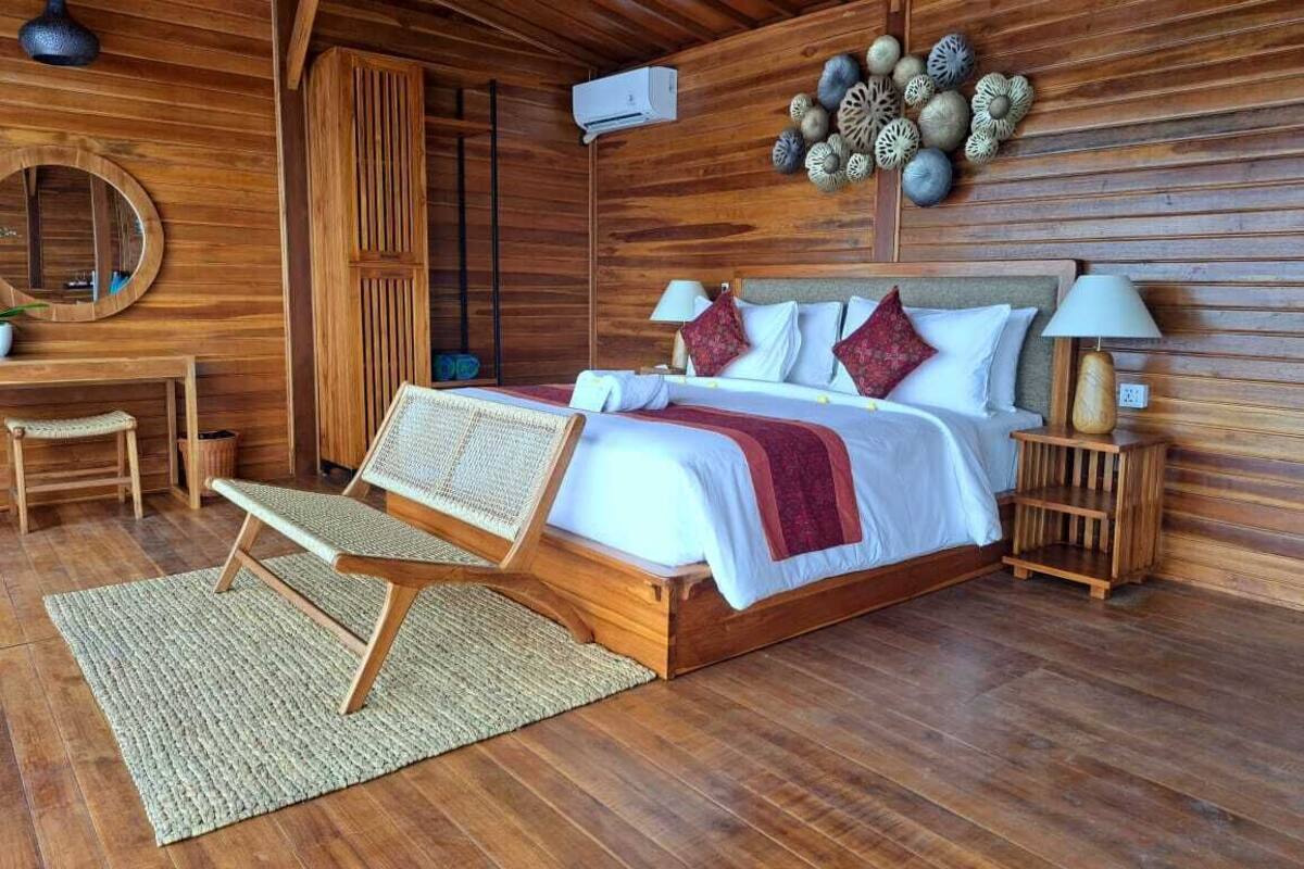 Une chambre à coucher aux murs lambrés, comprenant un lit, des tables de chevet, un fauteuil de lecture et un élément décoratif mural.