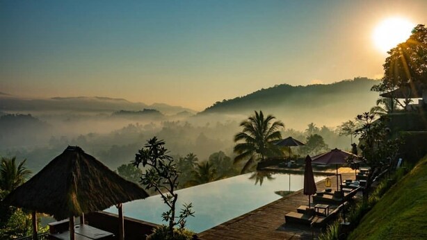 Um resort tranquilo com vista clara do nascer do sol sobre uma paisagem enevoada, piscina infinita e áreas de estar com guarda-sóis.