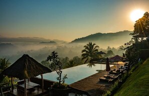 A serene resort with a clear view of the sunrise over a misty landscape, an infinity pool, and lounge areas with umbrellas. - Patal Kikian Villas (Sidemen)
