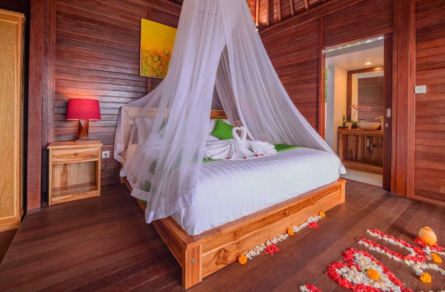 A wooden four-poster bed with a canopy, a bedside table with a lamp, and a painting on the wall.