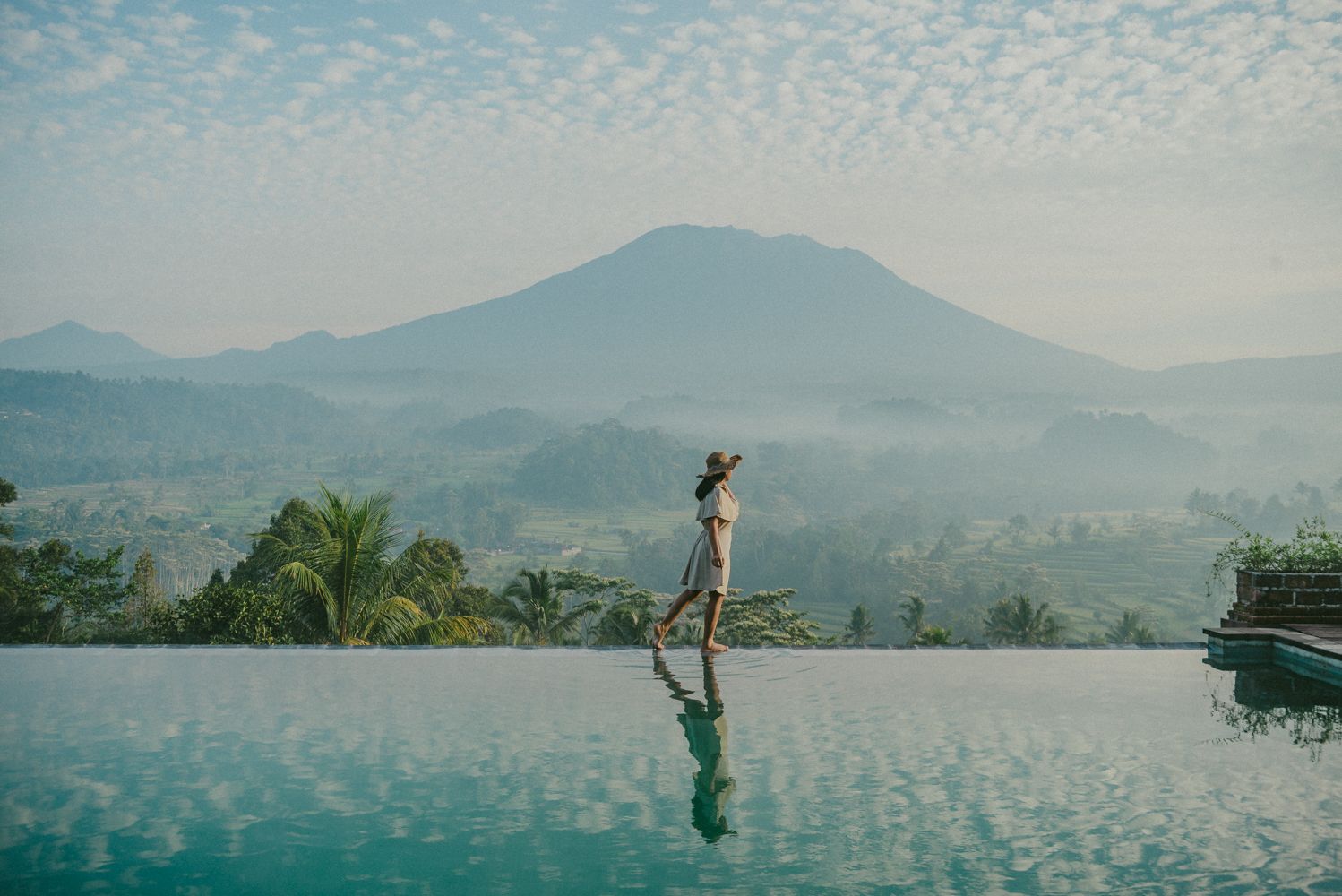 A person walking on a reflective infinity pool with a mountain in the background.