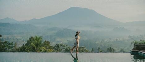 A person walking on a reflective infinity pool with a mountain in the background.