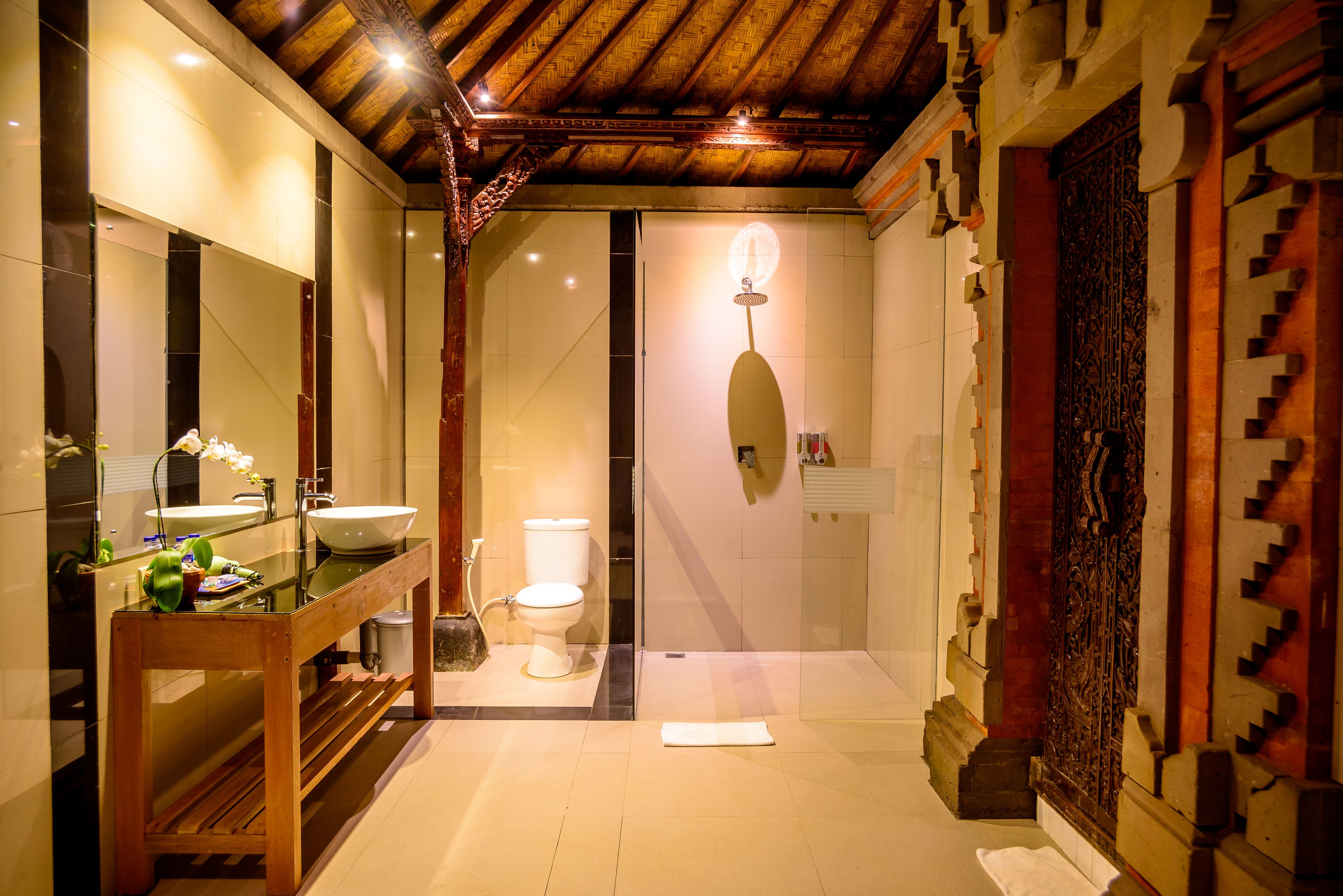 Un baño moderno con tocador de madera, un espejo grande, un lavamanos y un inodoro.