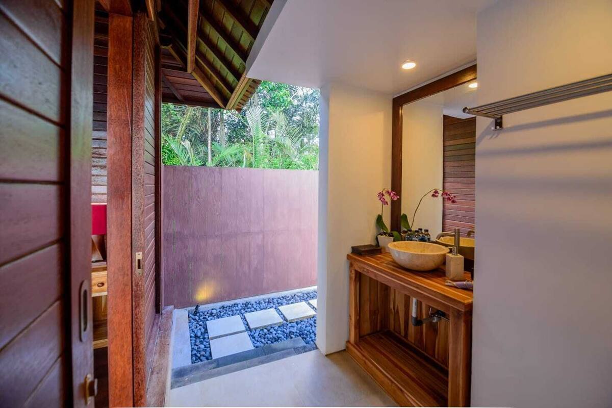 Une salle de bain avec un meuble-lavabo en bois, un grand miroir et une vue sur un jardin tropical.