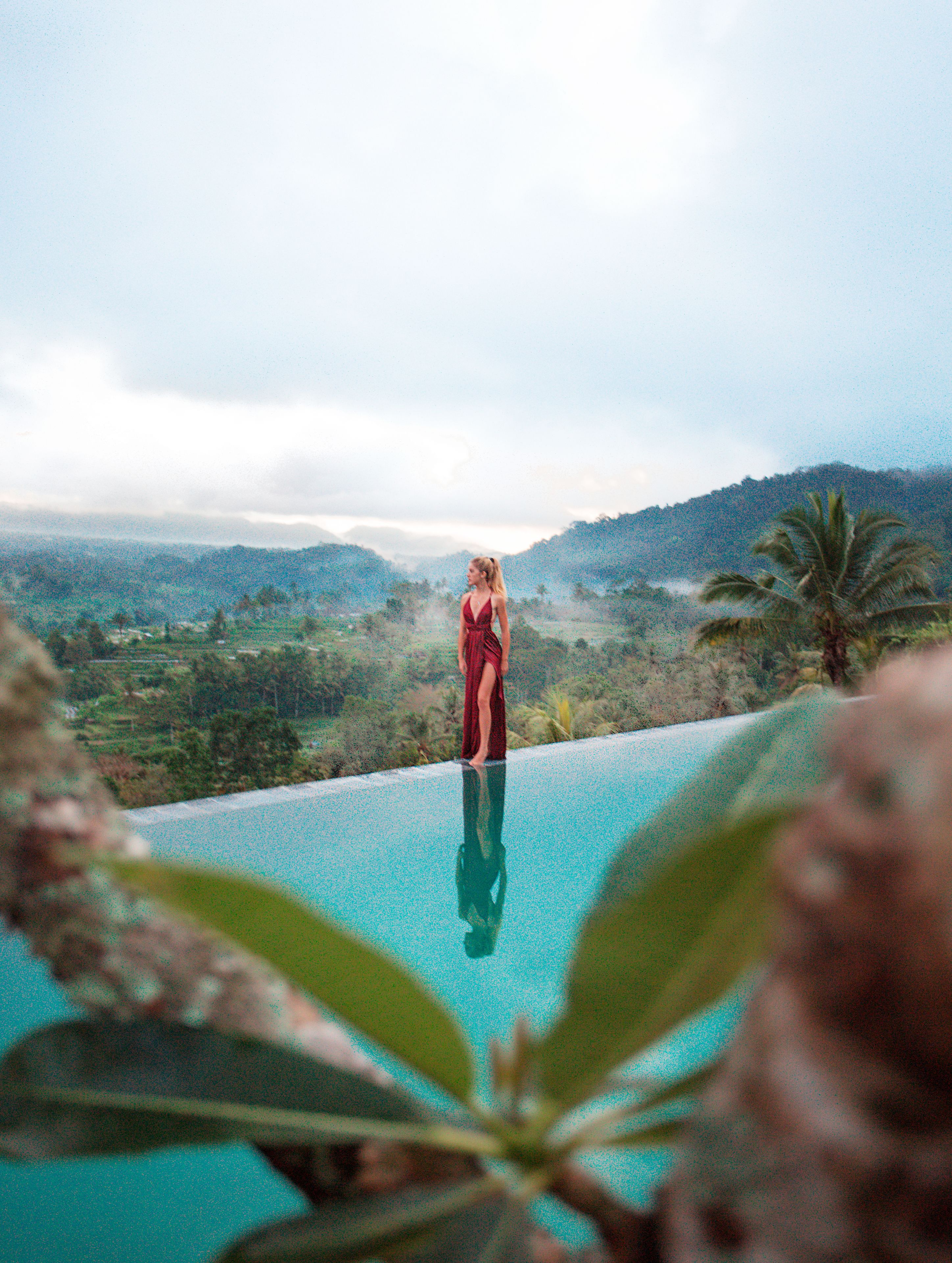 Una mujer de pie al borde de una piscina con vistas a un paisaje montañoso.