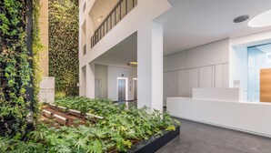 A modern indoor atrium with a central garden area, white reception desk, and a staircase leading to an upper level. - Front of Beach -Luxurious Residence (Tel Aviv)