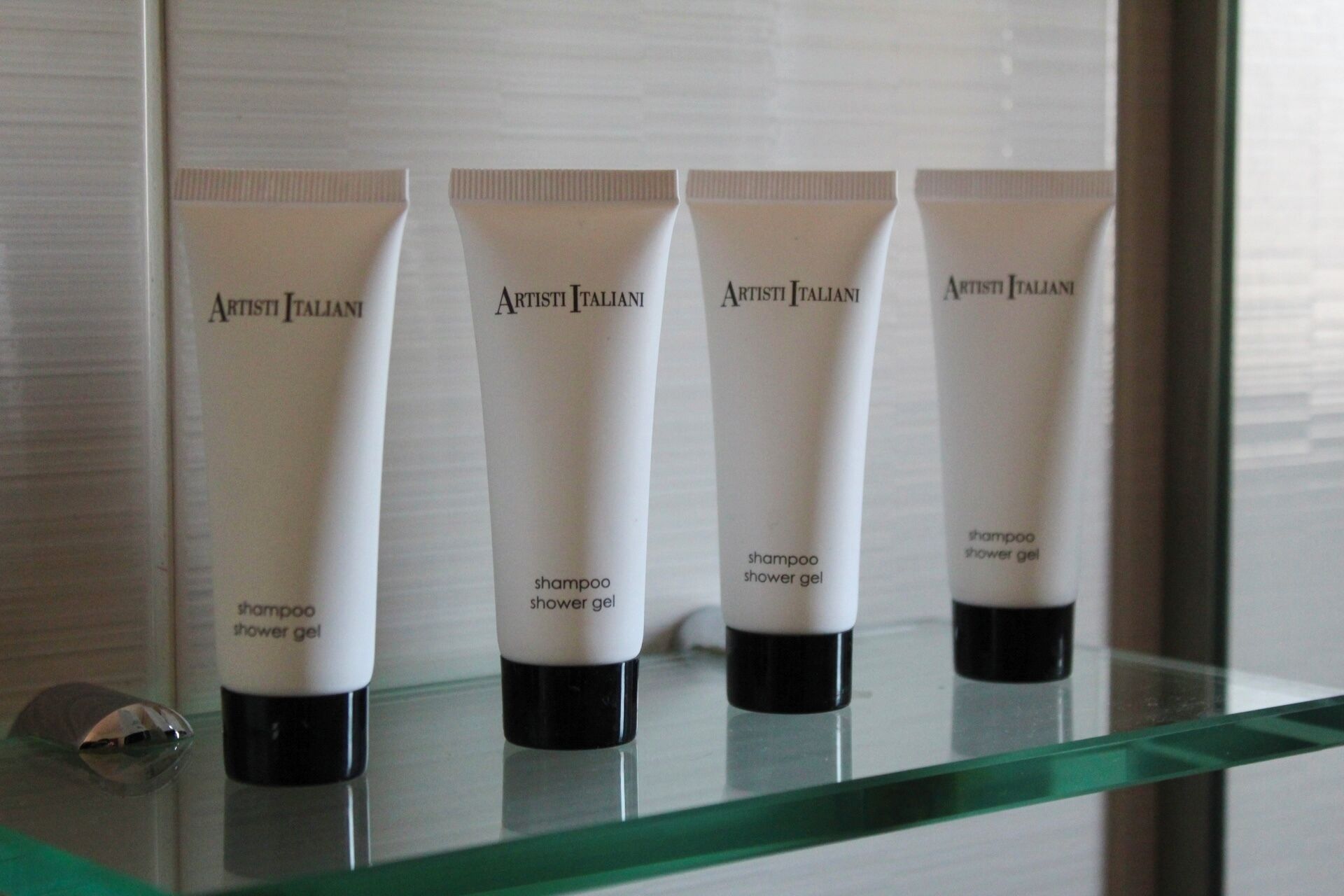 Four tubes of ArtistI Italian shampoo and shower gel on a glass shelf.