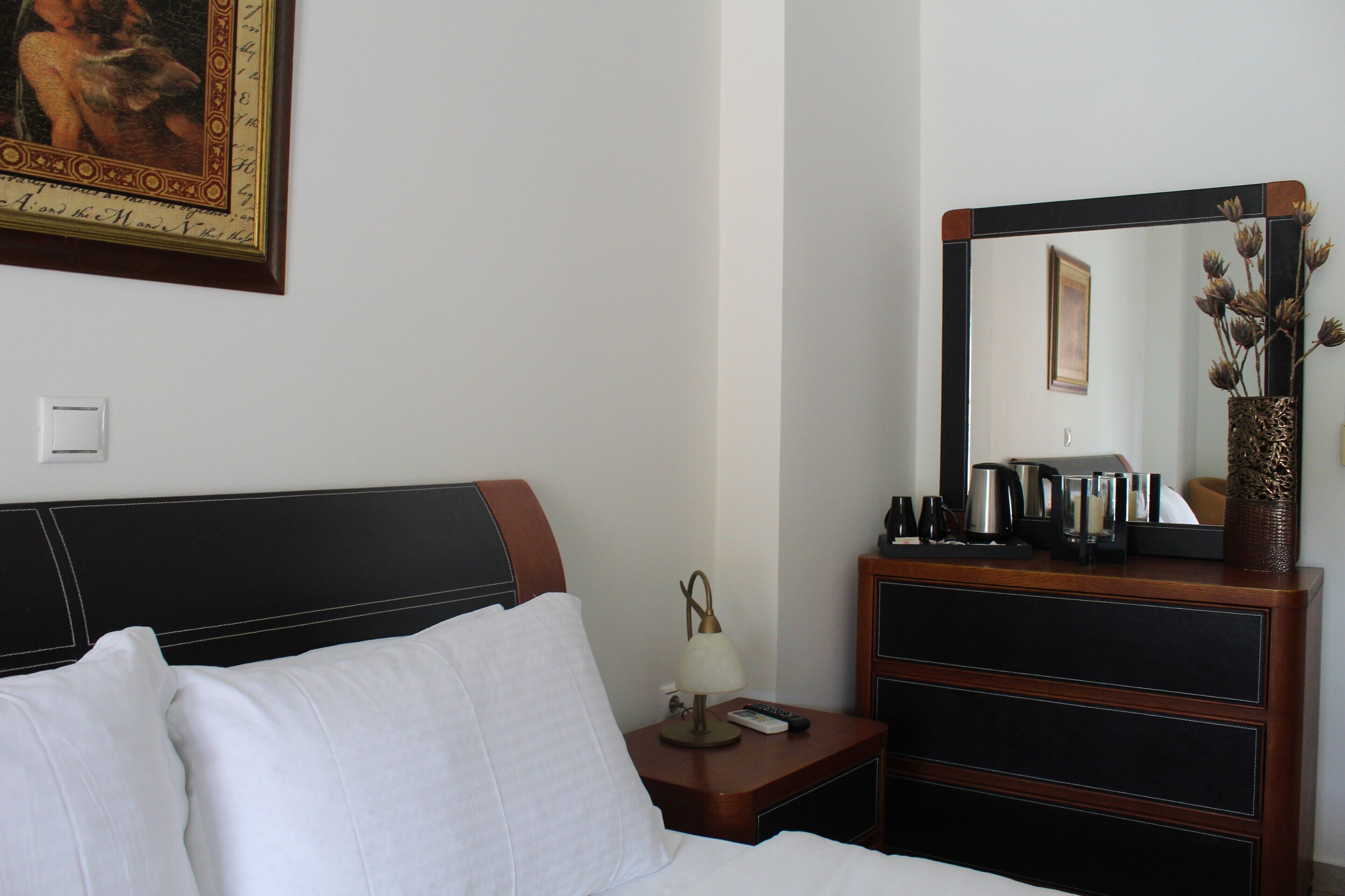 Una habitación de hotel con una cama, una mesita de noche con lámpara, un aparador y un espejo.