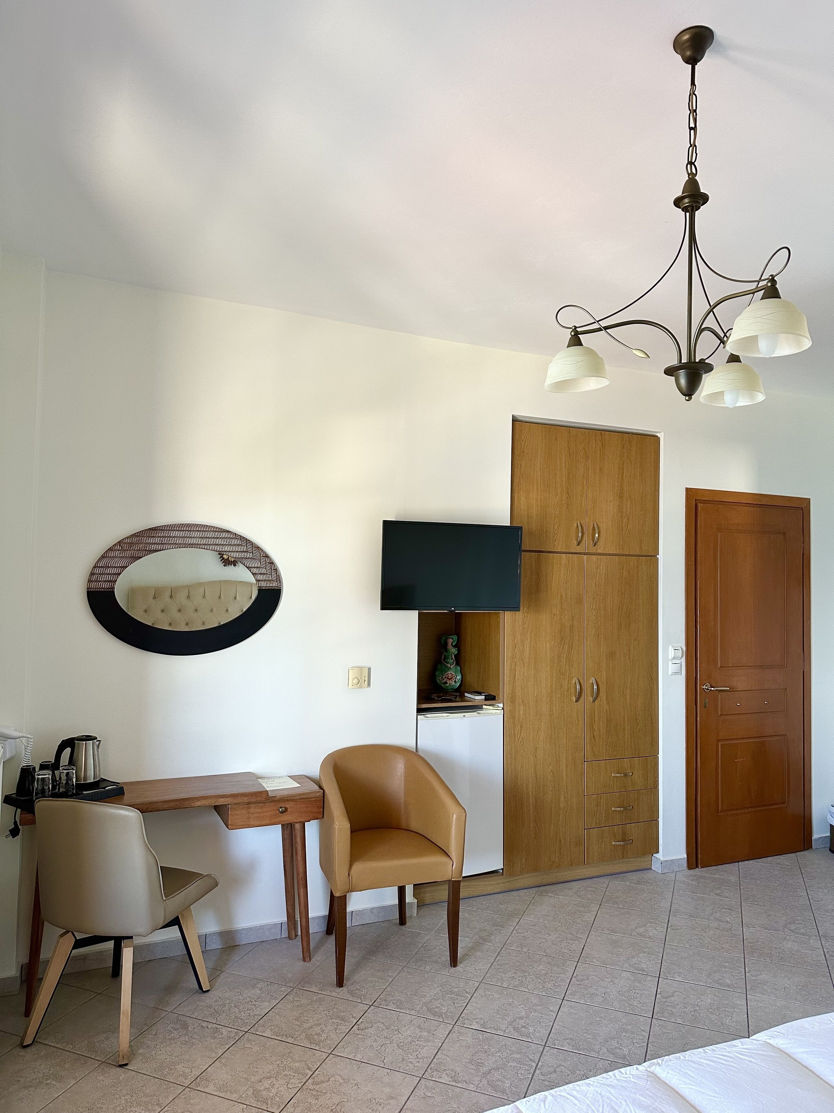 A room with a wooden desk, a chair, a television, a wardrobe, and a door.
