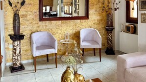 A living room with a stone wall, two white armchairs, a coffee table with decorative vases, a mirror, and a fireplace. - Sofotel (Pylos-Nestoras)