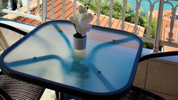 A balcony with a table and chairs, overlooking a coastal view with boats and a distant shoreline. - Sofotel (Pylos-Nestoras)