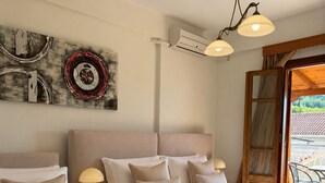 A hotel room with two beds, a ceiling fan, an air conditioning unit, a wall-mounted artwork, and a view of the outside. - Sofotel (Pylos-Nestoras)