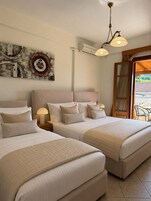 Habitación de hotel con dos camas, ventilador de techo, equipo de aire acondicionado, una obra de arte en la pared y vistas al exterior.