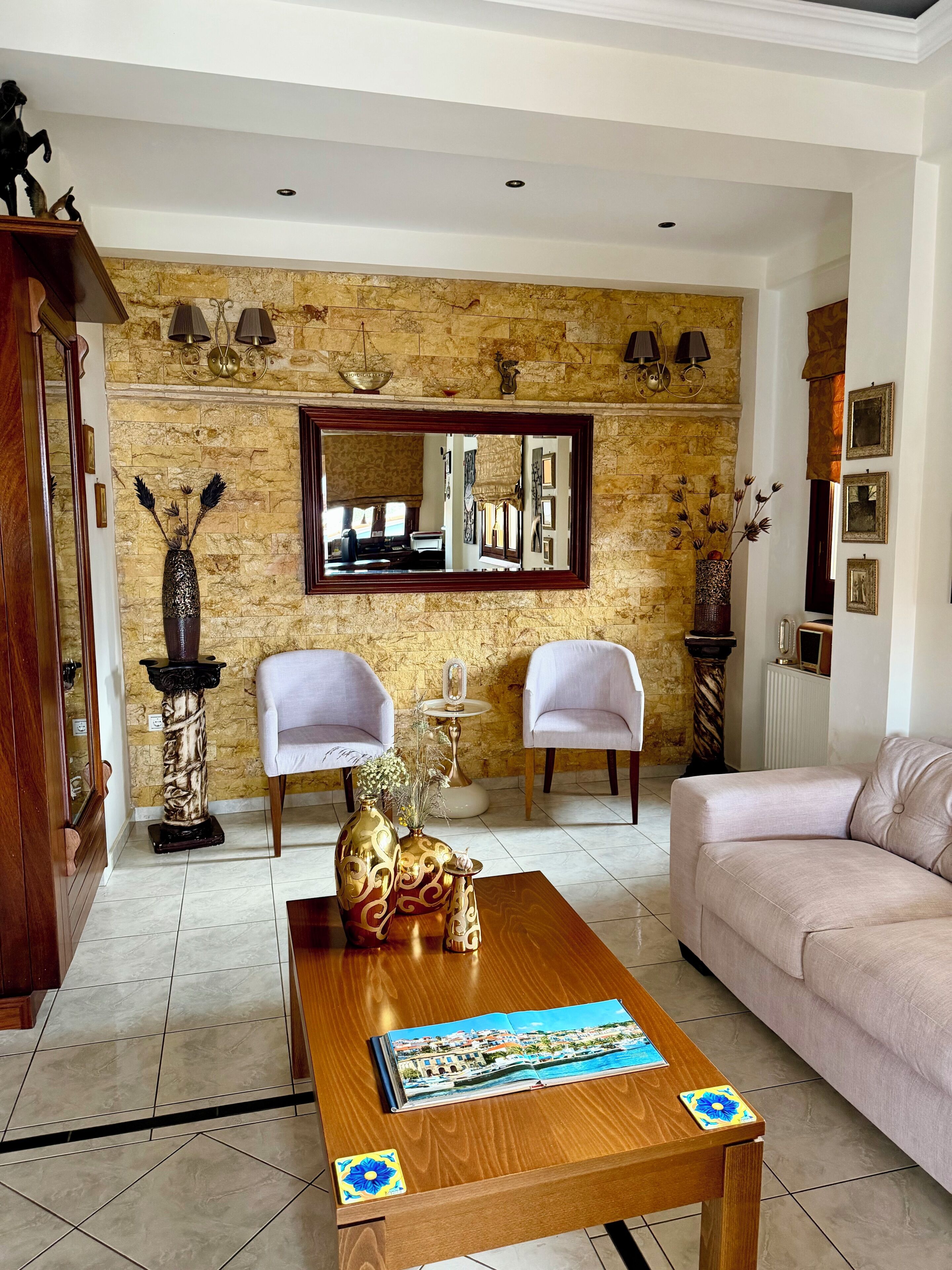 A living room with a stone wall, two white chairs, a wooden coffee table, and a beige sofa.