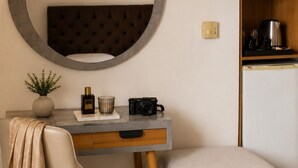 A modern room with a round mirror, a flat-screen TV, a desk with a chair, a small ottoman, and a kitchenette area. - Sofotel (Pylos-Nestoras)