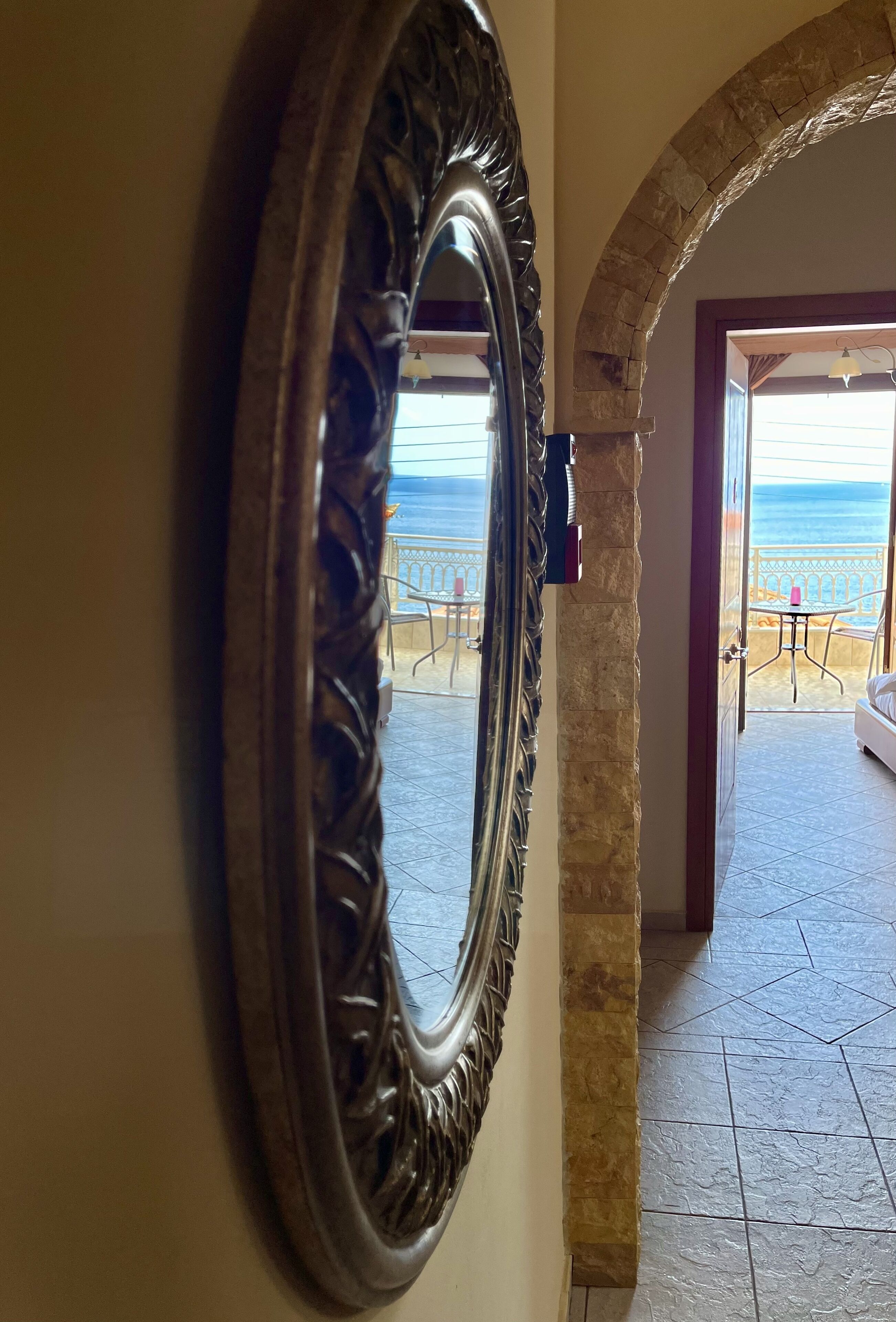 Un espejo con un marco decorativo, una pared de piedra y vistas a un balcón con mobiliario exterior.
