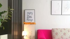 Una sala de estar moderna con un sofá rosa brillante, un otomano naranja mullido, una lámpara de pared y un cartel con una frase motivacional.