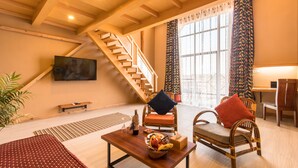 A spacious living room with a wooden staircase, a television mounted on the wall, and a dining area with chairs and a table.